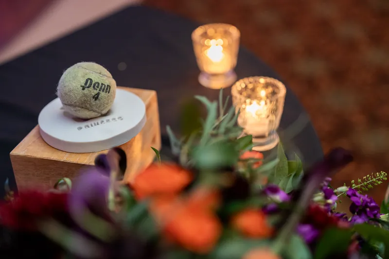 Place card reading "Penn" sits beside glowing candles and purple flowers on a reception table.