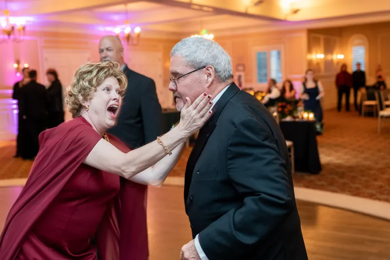 A woman in maroon touches a man's face as they share a surprised, joyful moment on the dance floor.