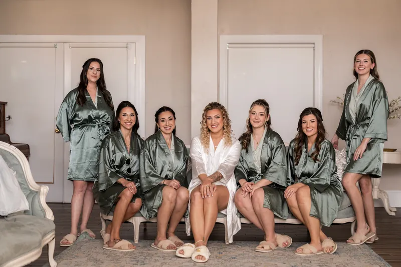 Bride with bridesmaids in matching sage robes sitting together during getting ready