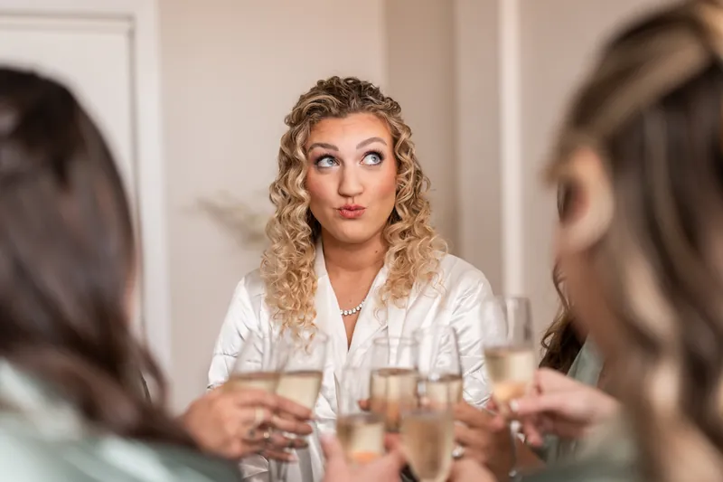 Bride making a playful face during champagne toast with bridesmaids