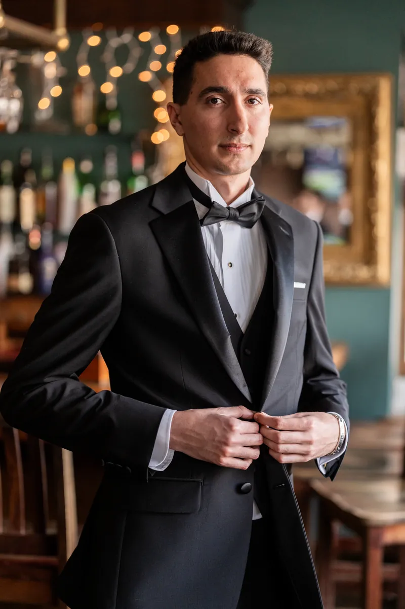Groom portrait buttoning his tux jacket at the bar