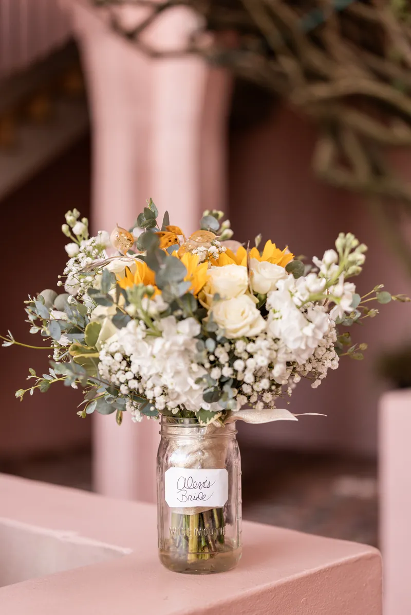 Bridal bouquet with sunflowers, white roses, eucalyptus, and baby's breath in mason jar labeled Alexis Bride