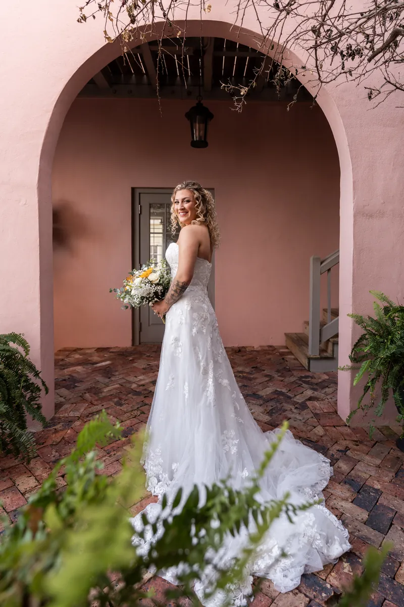 Bride portrait in pink courtyard archway at The White Room holding sunflower bouquet