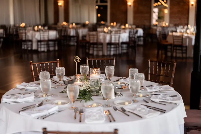 Reception table setting with candlelight, chiavari chairs, greenery, and exposed brick walls