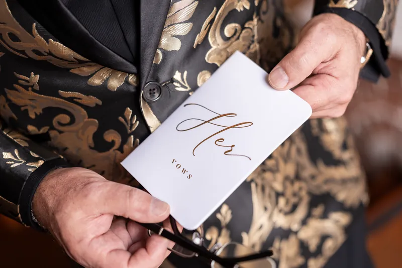 Hands holding Her Vows booklet in gold brocade jacket