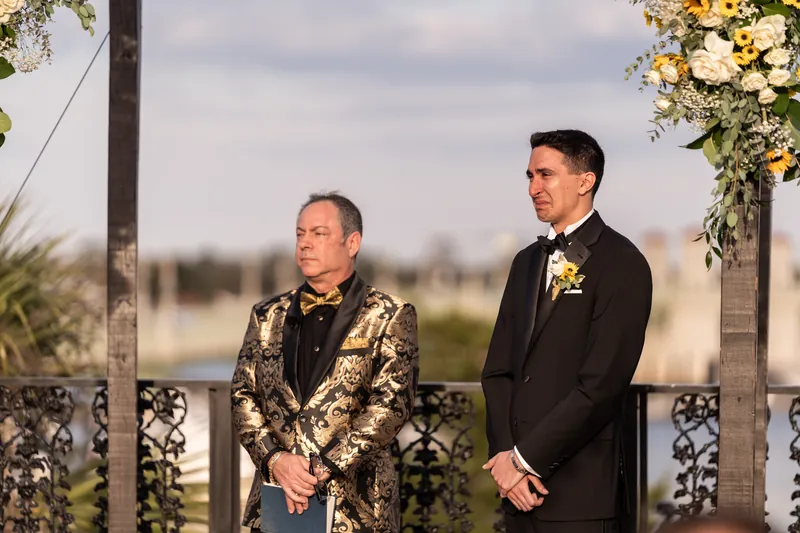 Groom getting emotional at the altar next to officiant with bayfront behind them