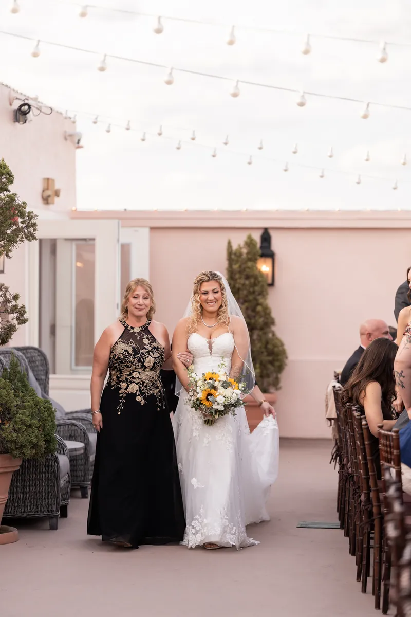 Bride walking down the aisle with her mother on The White Room rooftop under string lights