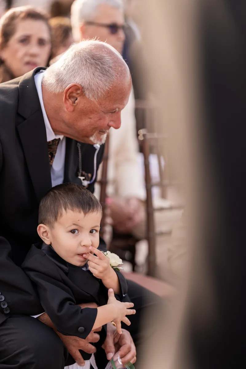 Young ring bearer sitting on grandfather's lap during rooftop ceremony