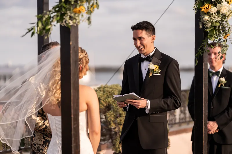 Groom reading his vows and smiling at bride during rooftop ceremony
