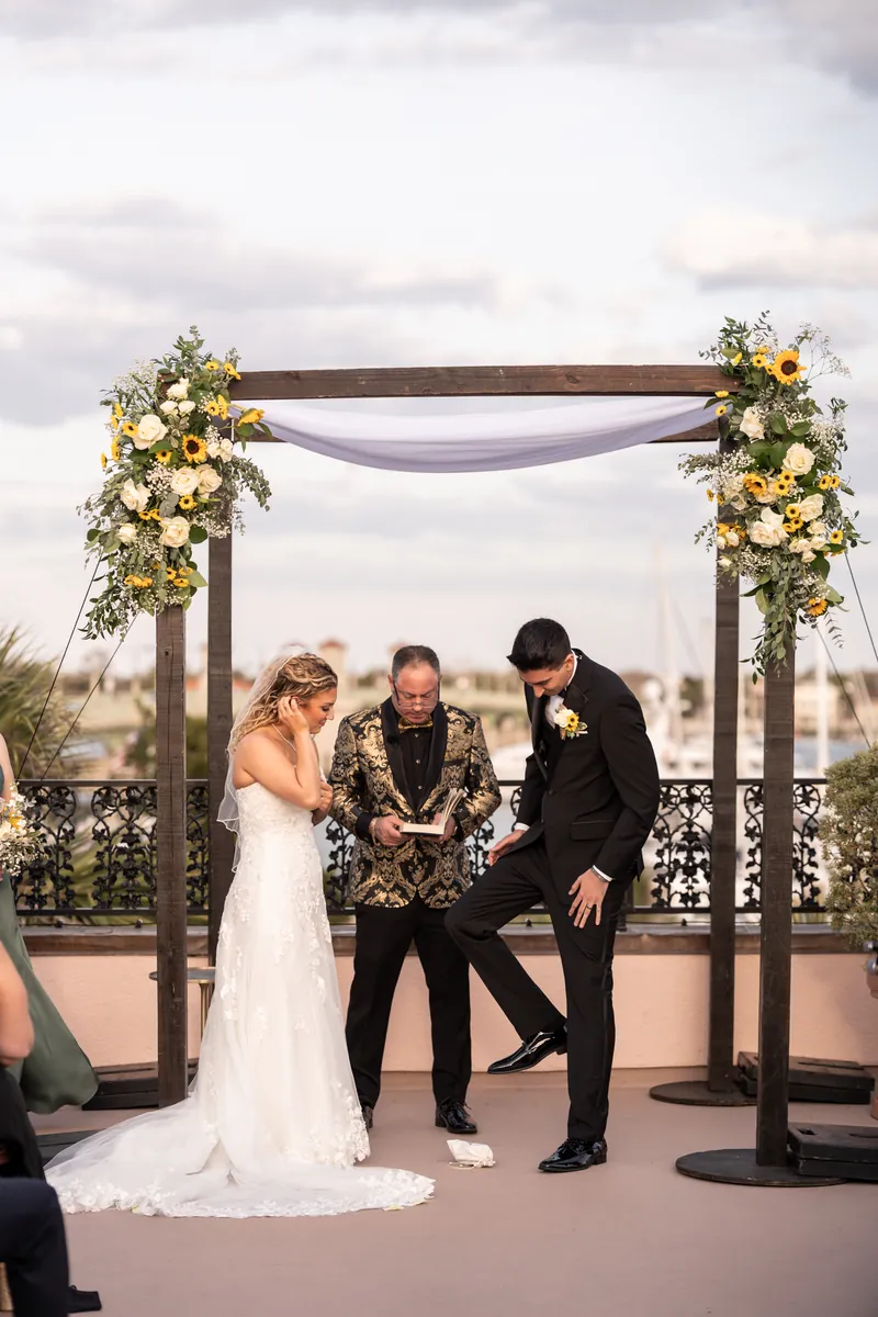 Bride and groom stomping the glass under ceremony arch with Matanzas Bay behind them