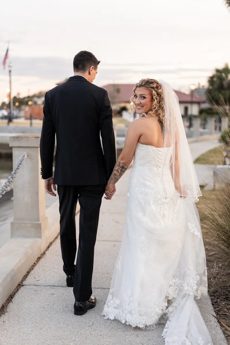 Bride looking back over her shoulder while walking hand in hand along the St. Augustine bayfront