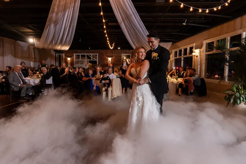 First dance on cloud of fog in reception hall with guests watching from candlelit tables