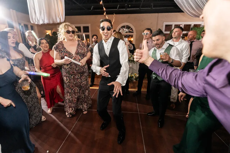 Groom dancing in sunglasses with guests and glow sticks on the dance floor