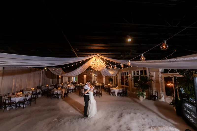 End-of-night couple portrait in empty reception hall with fog, chandelier, and string lights