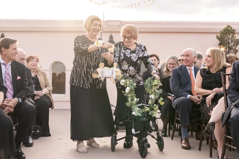 Two women walk alongside a small child in a stroller decorated with white flowers at The White Room.