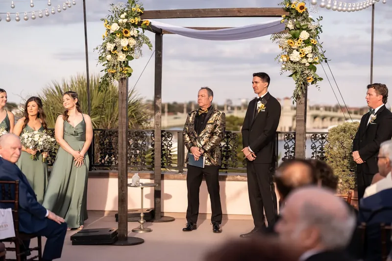 Dino stands at the altar beneath a floral-draped pergola as guests watch the ceremony unfold at The White Room, St.