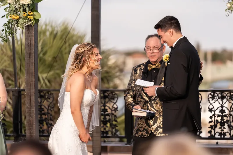 The officiant speaks to Alexis and Dino during their ceremony, with palm trees and St. Augustine's skyline visible behind