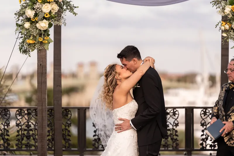 Dino dips and kisses Alexis under the pergola as guests watch their first kiss as a married couple.