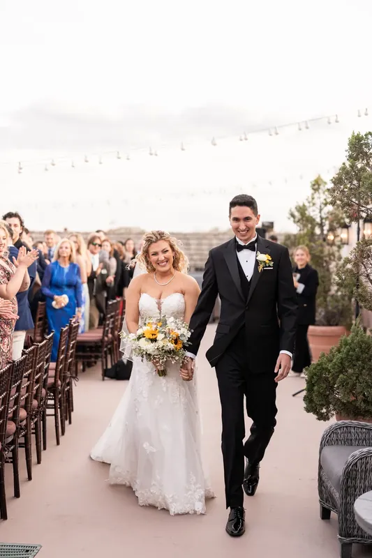 Alexis and Dino walk back up the aisle together after their ceremony, smiling at guests lining both sides.