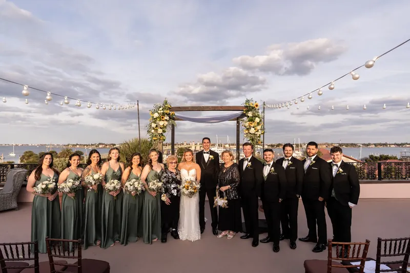 Alexis and Dino stand center with their wedding party on The White Room's rooftop, flanked by a wooden arch with floral