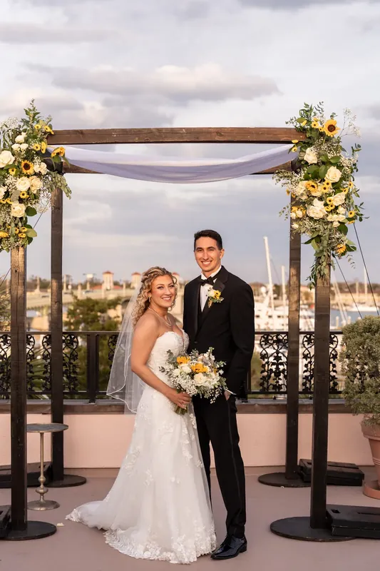 Alexis and Dino pose beneath a flower-adorned wooden arch overlooking St. Augustine's cityscape at The White Room.