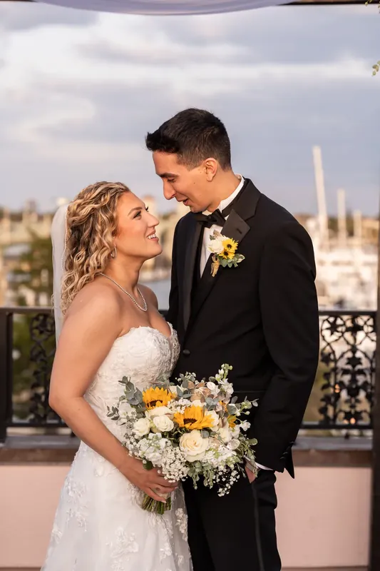 Alexis and Dino gaze at each other on the rooftop, with the city skyline and water visible behind them.