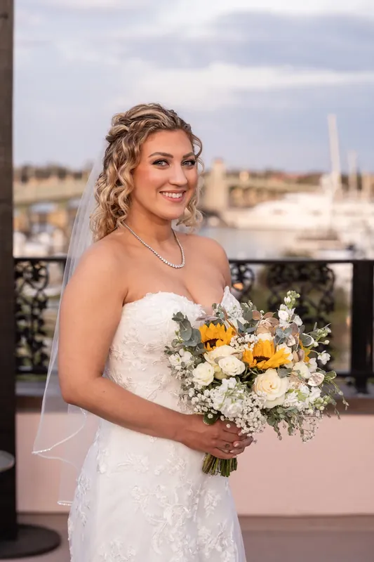 Alexis holds her white and yellow bouquet, smiling toward the camera with St. Augustine's waterfront in the background.
