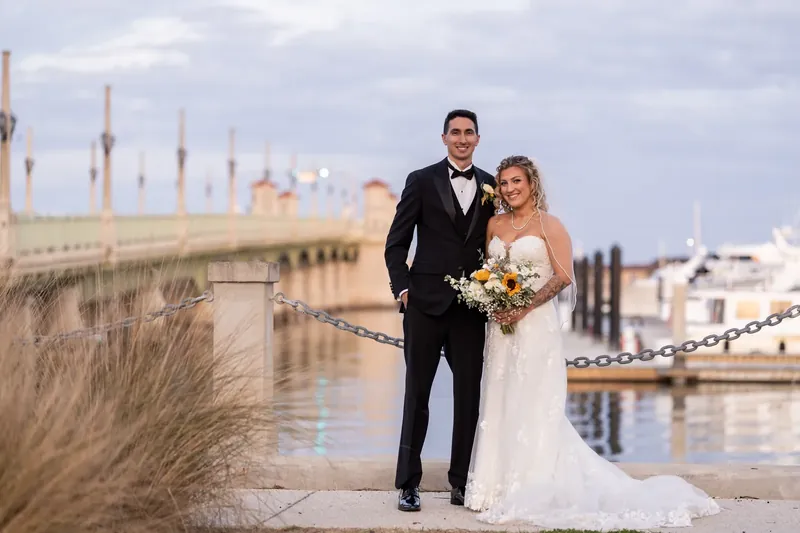 Alexis and Dino walk along the St. Augustine Bayfront, holding hands with historic buildings and water visible behind them.