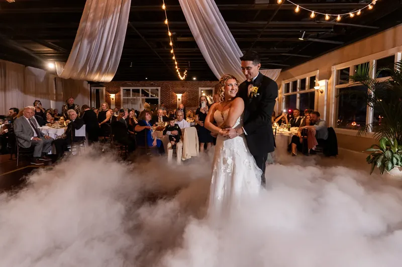 Alexis and Dino dance through billowing fog on The White Room's outdoor venue as guests watch from surrounding tables.