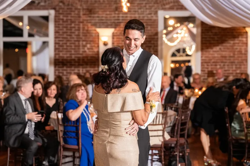Dino spins Alexis in her champagne-colored dress on the dance floor as guests watch from the brick-walled venue.