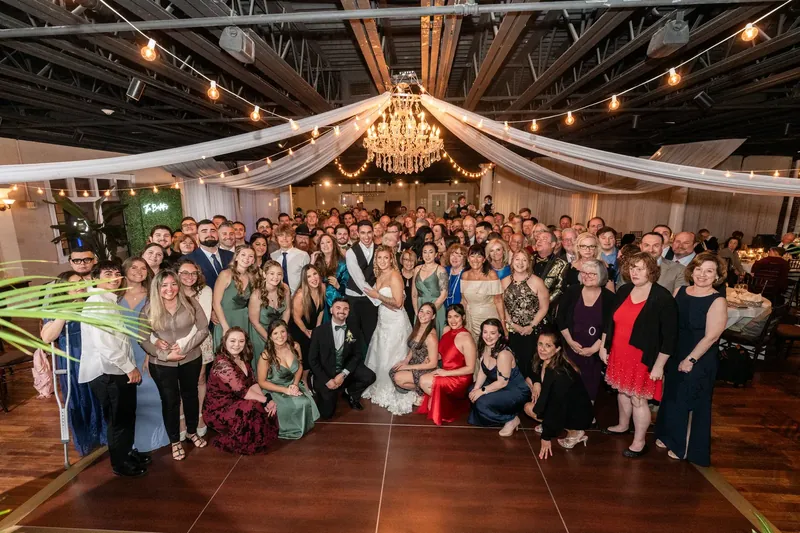 Alexis and Dino stand with their wedding guests under a chandelier and draped fabric inside The White Room, St. Augustine.