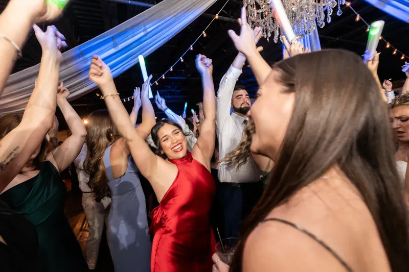 Wedding guests raise their arms and cheer while holding a glow stick during the dance celebration.