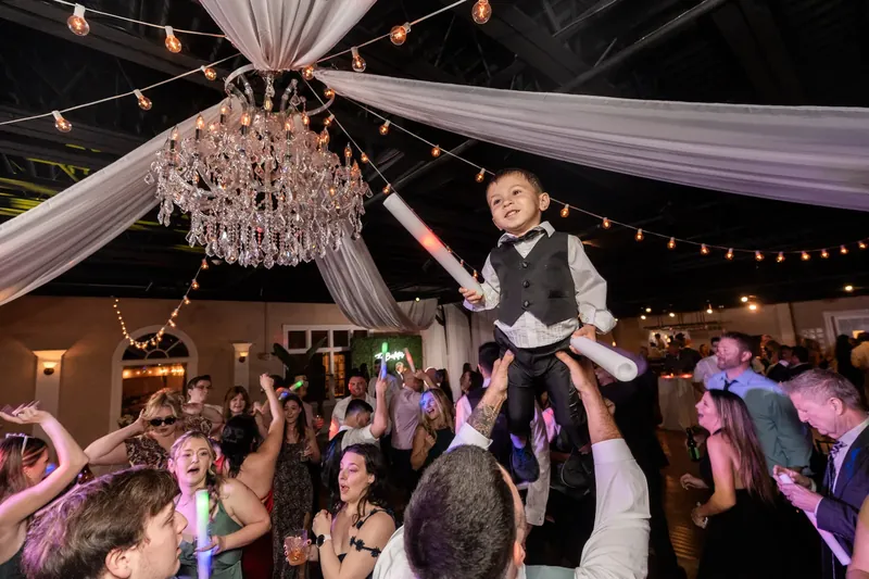 Guests lift Dino into the air beneath a crystal chandelier and draped fabric at The White Room's reception.