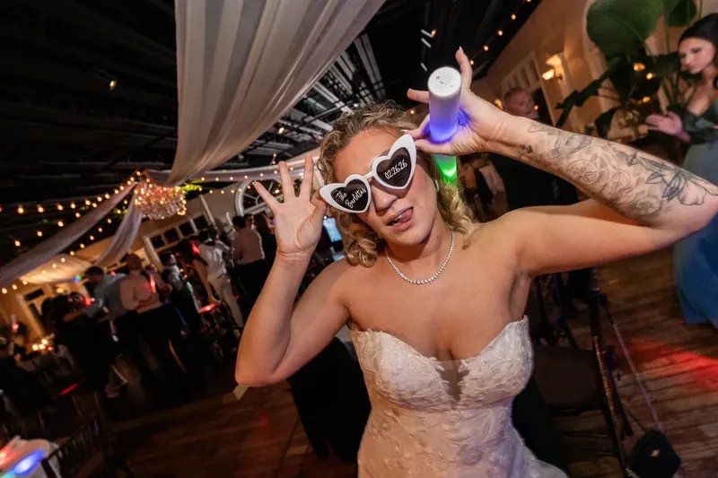 Alexis celebrates on the dance floor wearing oversized novelty sunglasses and a beaded white dress.