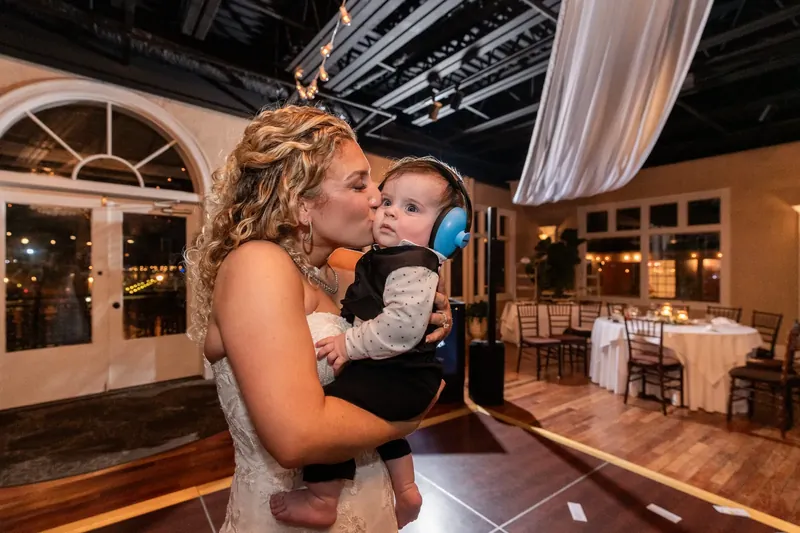 Alexis holds a young child while dancing, wearing her strapless beaded gown in the softly lit reception space.