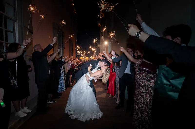 Alexis and Dino kiss beneath a canopy of raised sparklers while guests line both sides of the walkway.