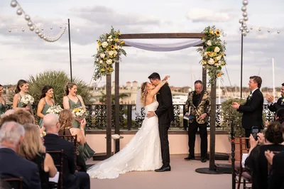 St. Augustine wedding photographer - bride and groom first kiss at rooftop ceremony at The White Room with sunflower arch and bayfront views