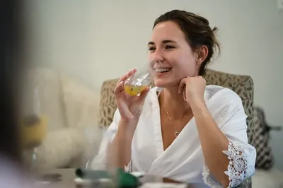 Woman in white lace blouse smiling while holding champagne glass indoors