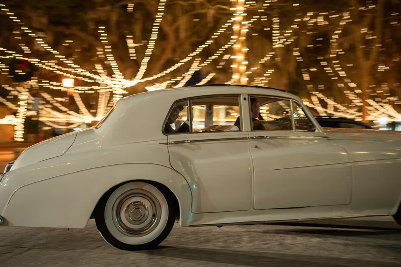 A cream-colored vintage car sits beneath glowing strung lights at The Treasury on the Plaza in St. Augustine.
