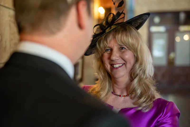 A woman in a purple dress and fascinator smiles while facing a man in a suit at The Treasury on the Plaza.