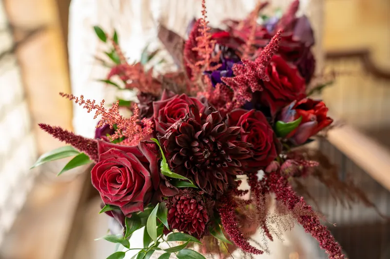 Deep red and burgundy roses with astilbe and greenery form a dense bridal bouquet in natural light.