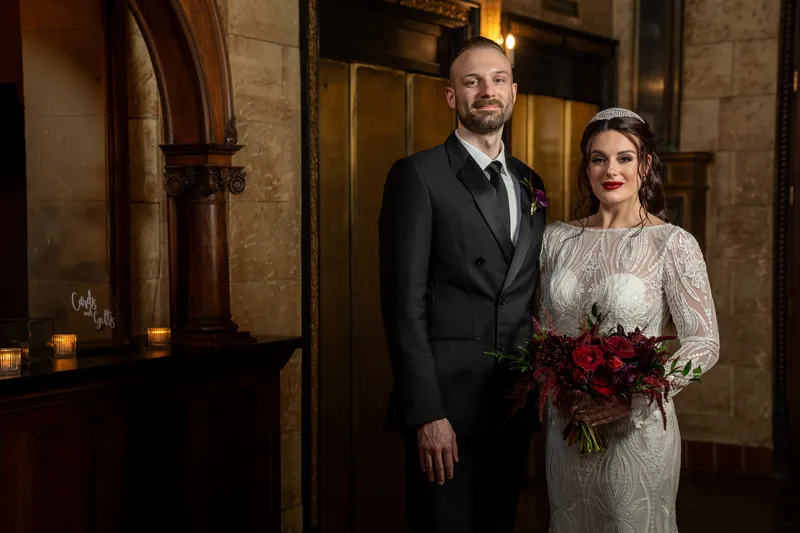Sam in a dark suit stands beside Alyson in a beaded ivory gown under arched stone doorways.
