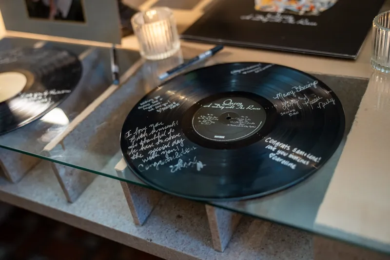 Black vinyl records with handwritten messages rest on a glass table as a guest book.