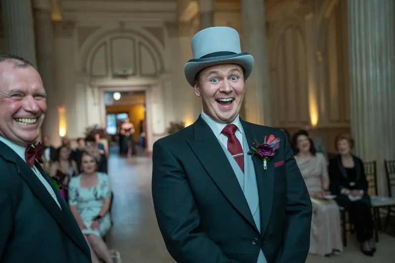 Sam grins widely in a light blue top hat and dark suit at The Treasury on the Plaza.
