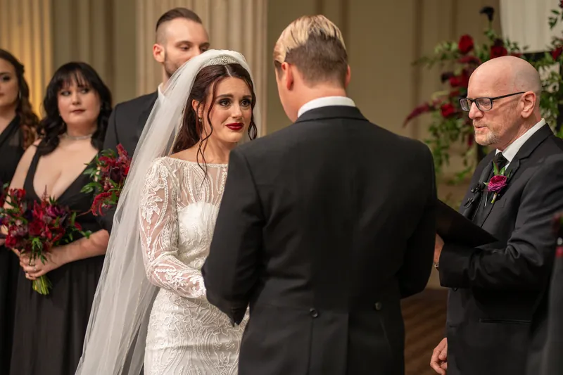 Alyson holds hands with an officiant while Sam looks on during their ceremony at The Treasury on the Plaza.