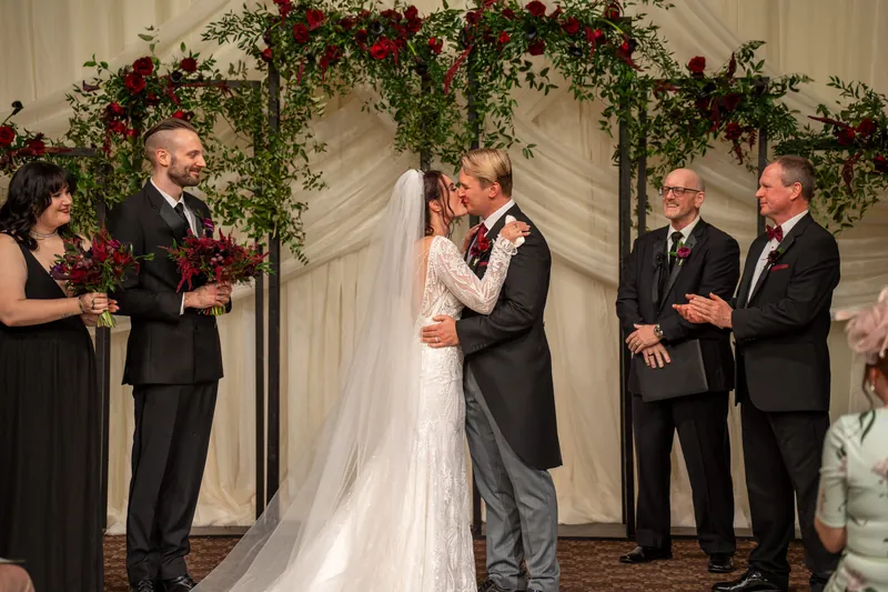 Sam kisses Alyson under a garland-draped arch as wedding guests look on at The Treasury on the Plaza.