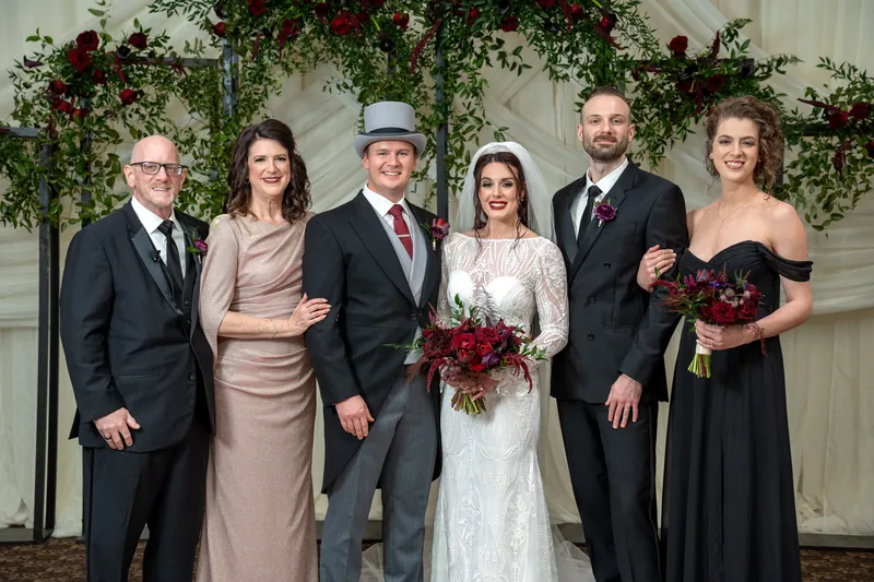 Alyson stands with five family members in formal wear, holding a deep red bouquet at The Treasury on the Plaza.