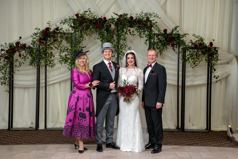 Alyson poses with three relatives—one in a vibrant magenta dress—beneath the ceremony arch at The Treasury on the Plaza.