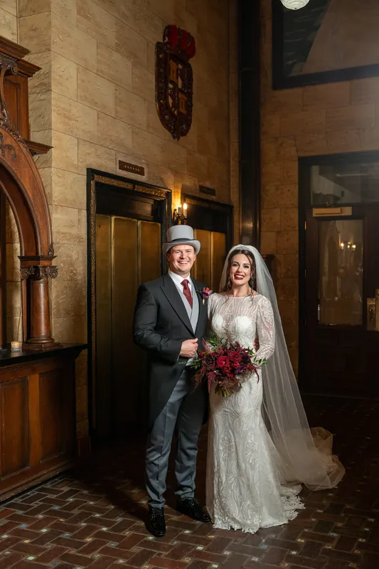 Sam and Alyson pose beneath ornate archways holding a deep red bouquet at The Treasury on the Plaza.