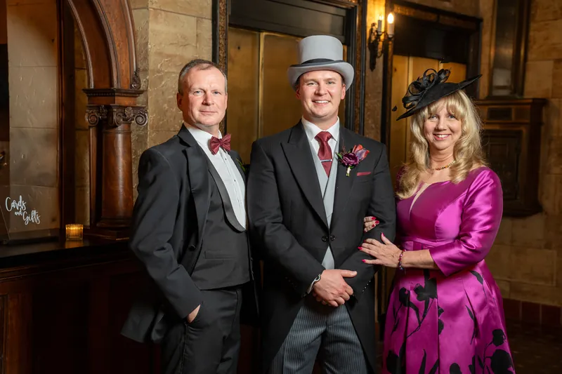 Two men in dark suits and a woman in magenta stand together in the historic hallway.